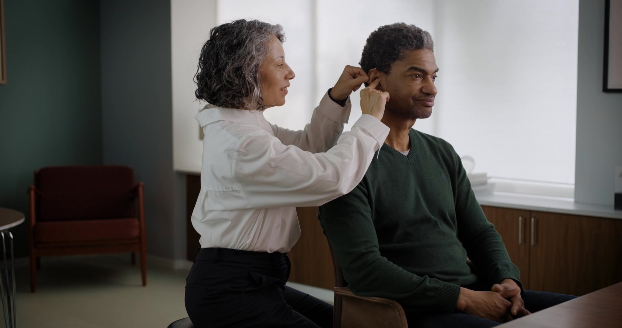 A hearing care professional fitting a hearing aid behind a client's ear