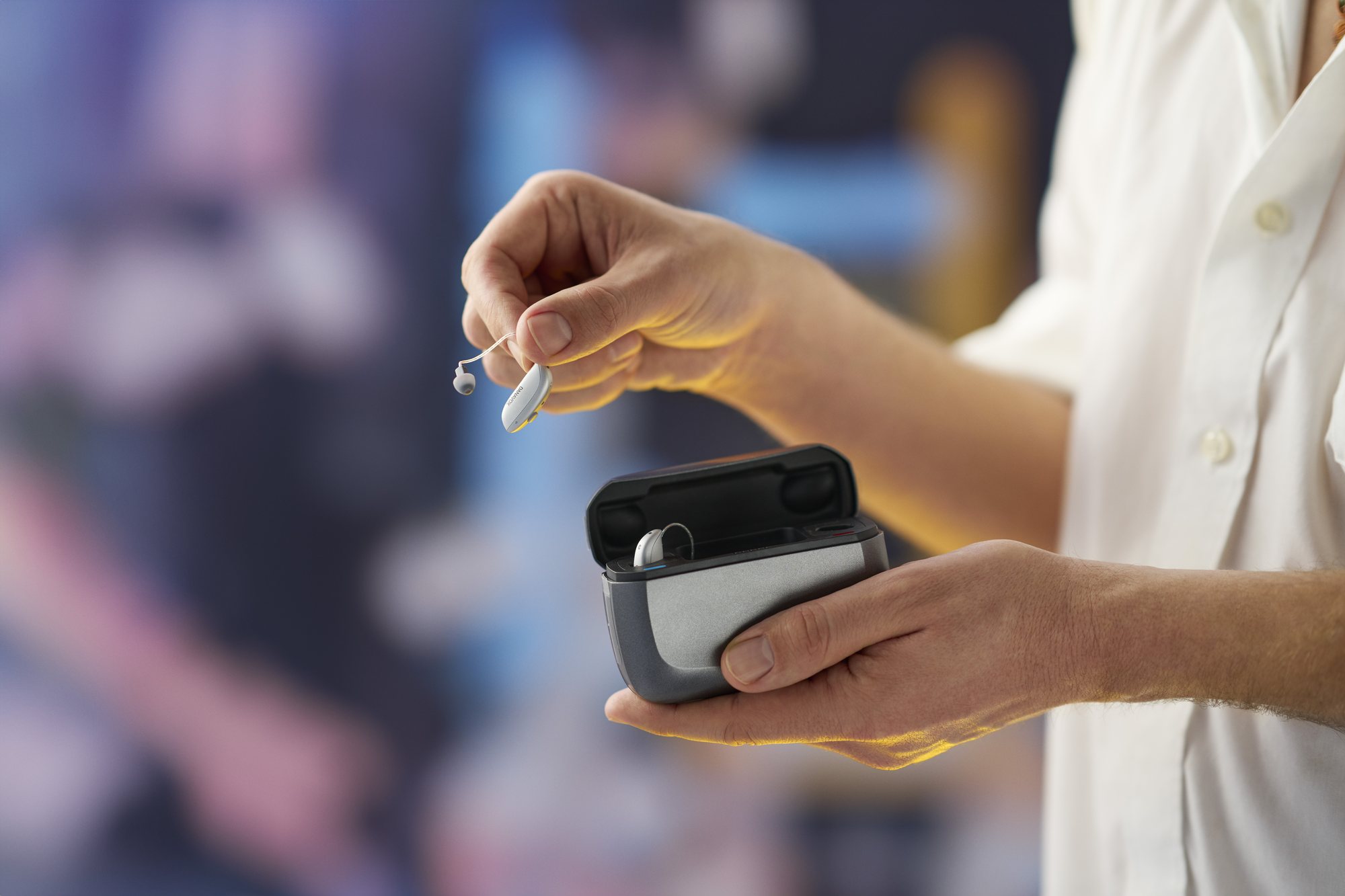 A Danavox hearing aid and its charging case in hand